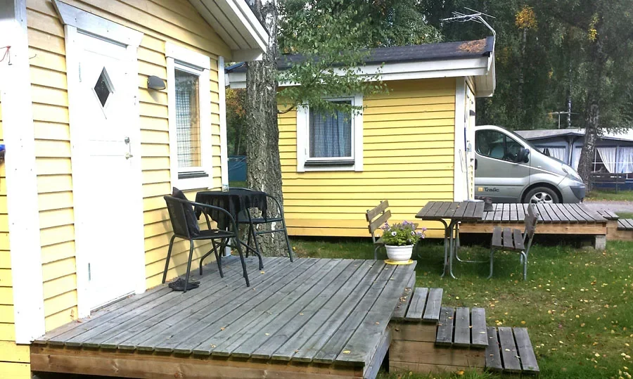 Gul stuga med altan, bord och stolar samt skåpbil intill