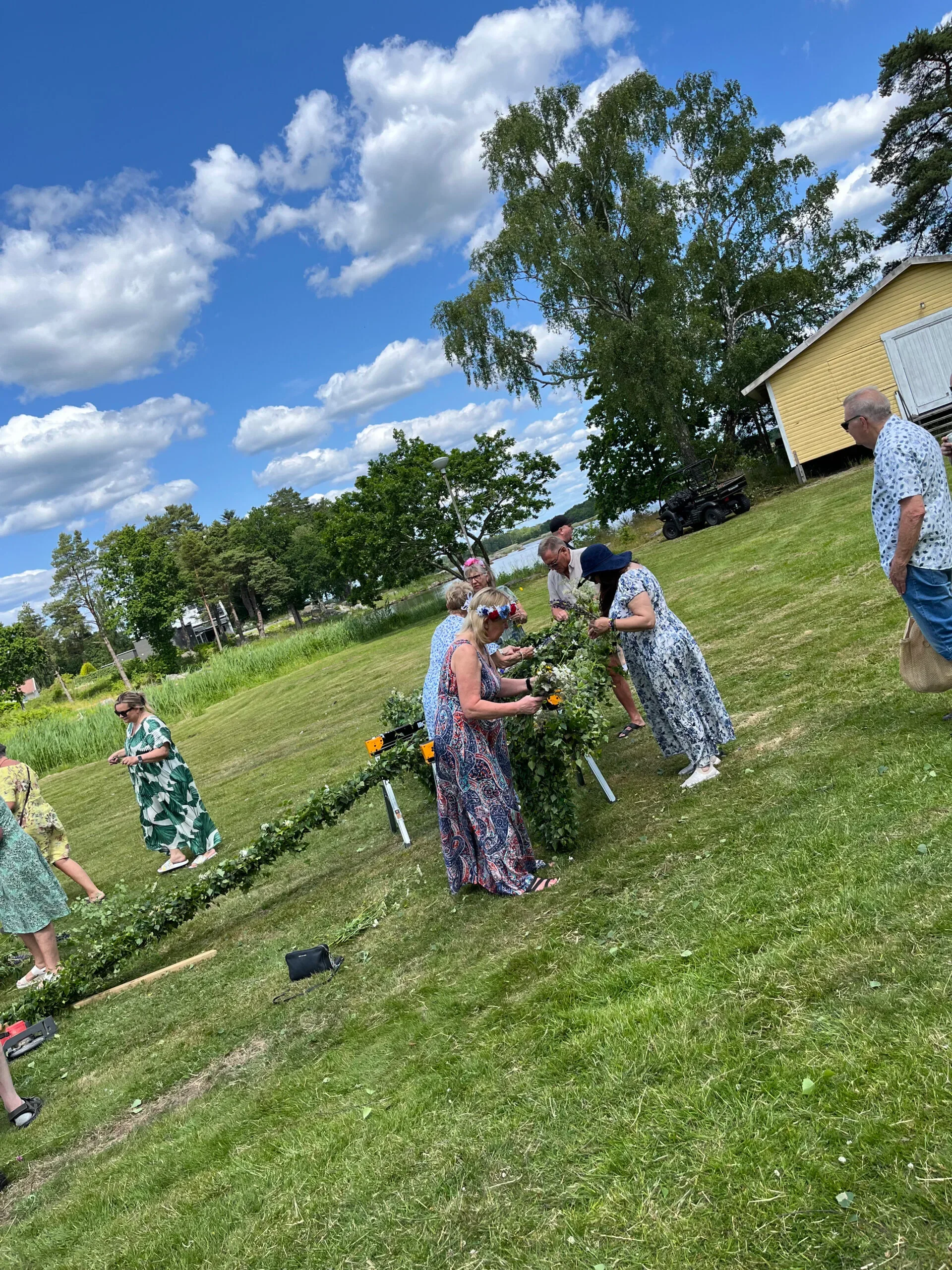 Människor klär midsommarstång under blå himmel