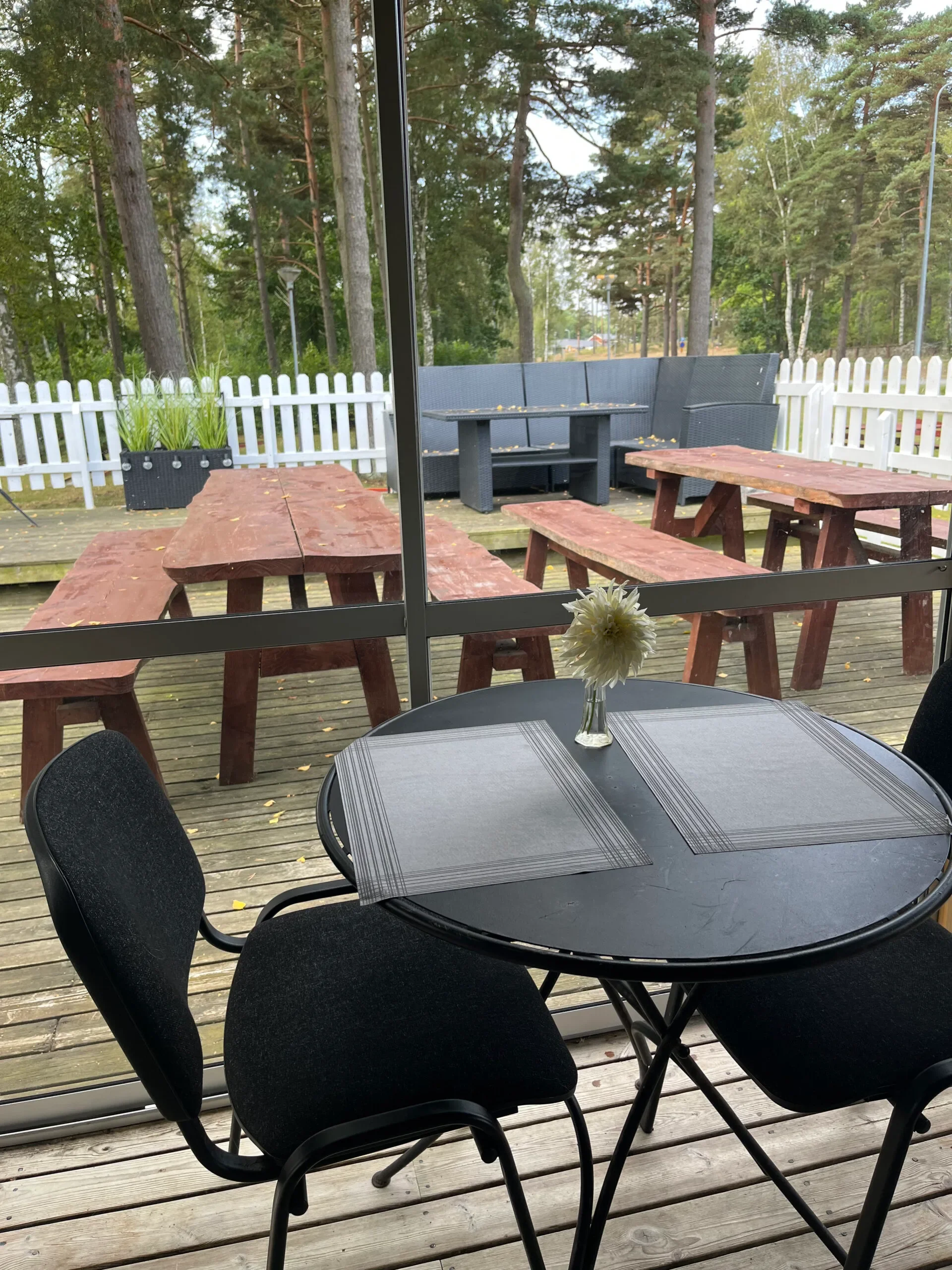 Uteservering med picknickbord och stolar på trädäck vid vitt staket