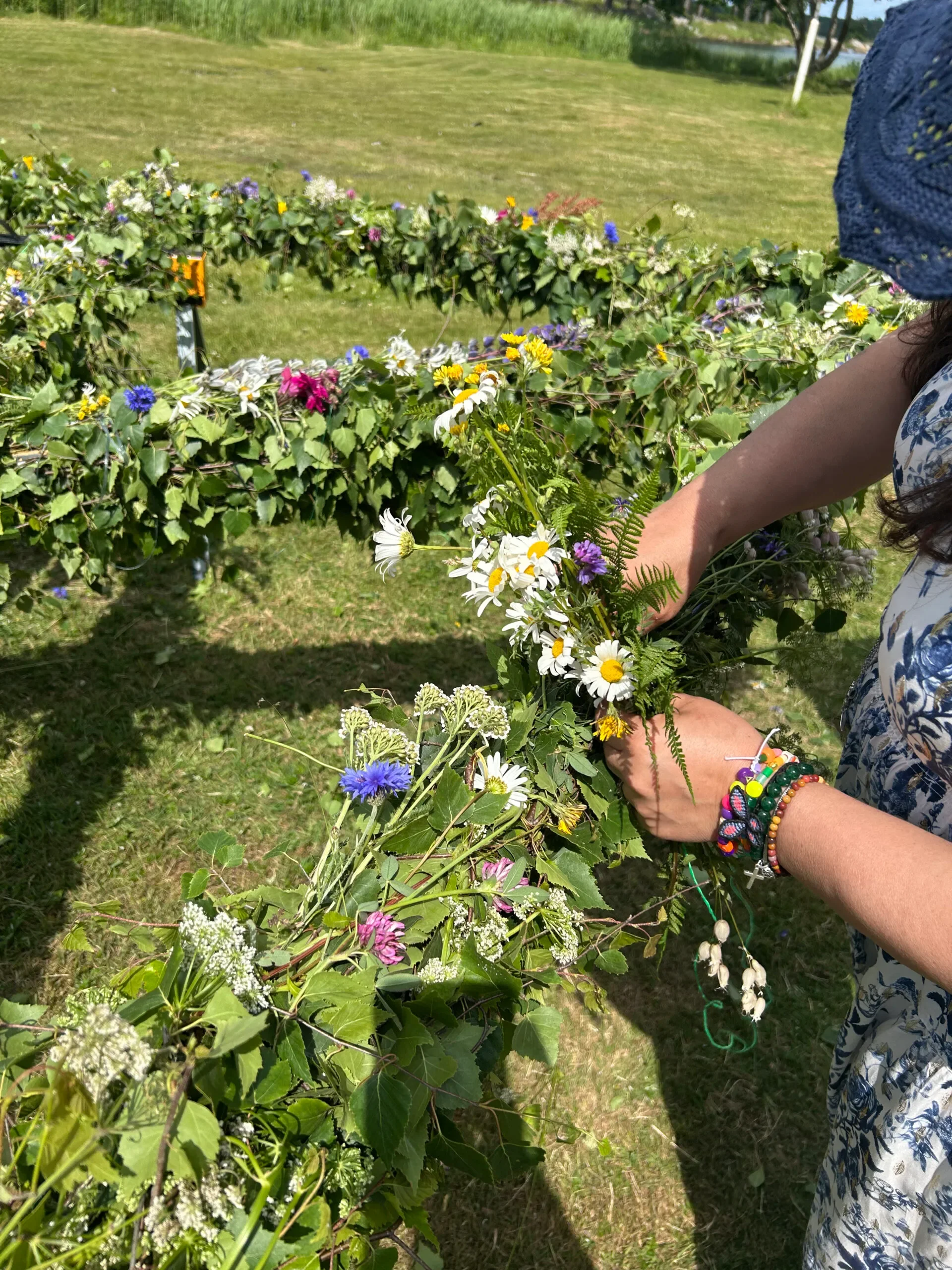 Panorama över festäng med folk, midsommarstång och gul byggnad