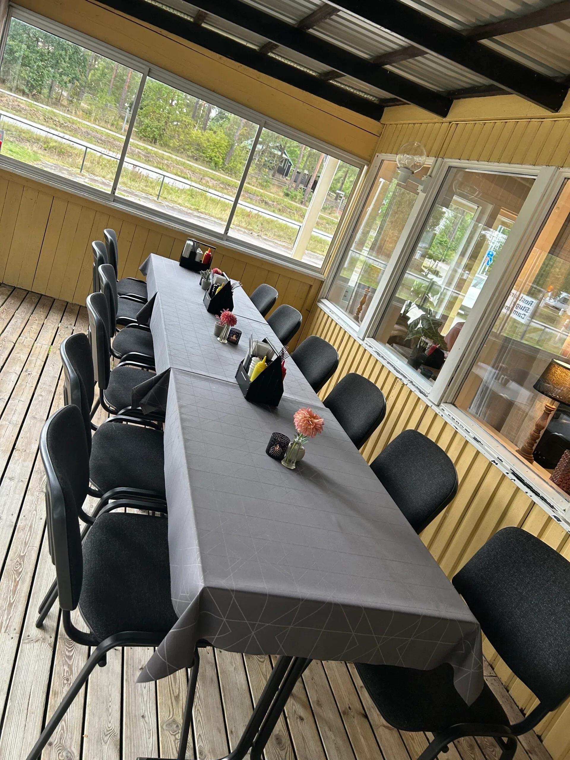 Långbord med grå duk och svarta stolar på inglasad veranda