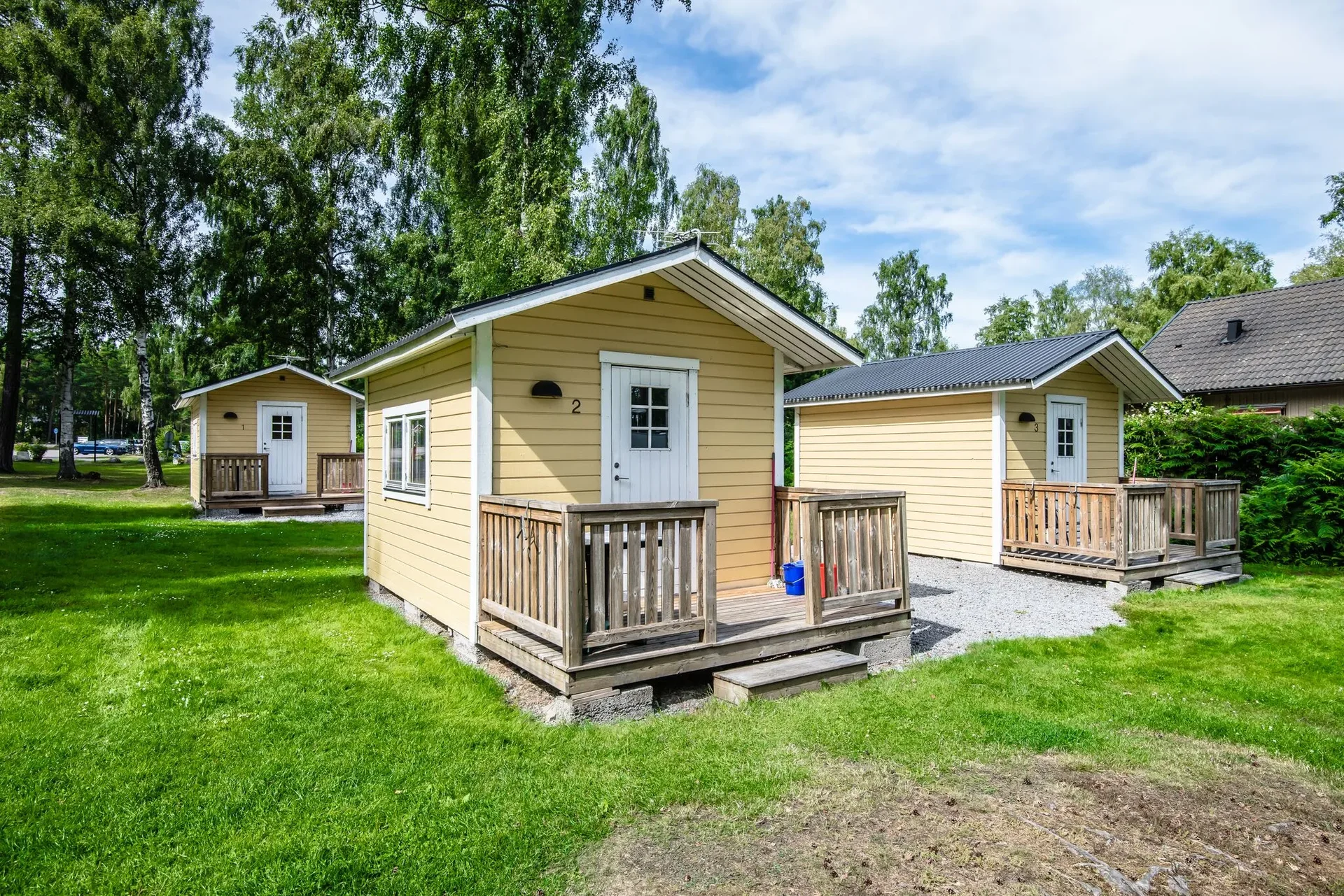 Gul stuga med vit veranda och räcke på gräsmatta