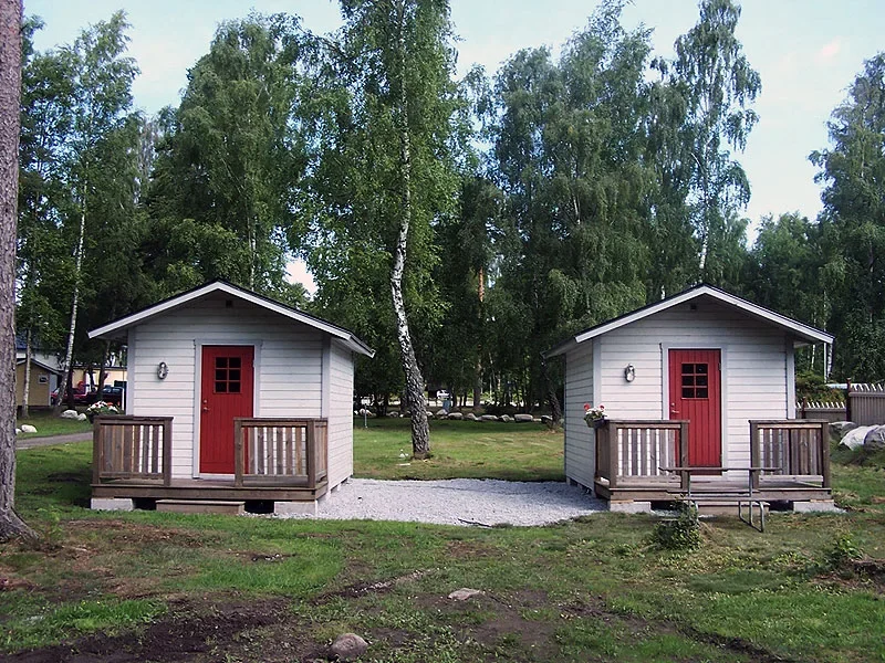 Två små vita stugor med röda dörrar bland björkar